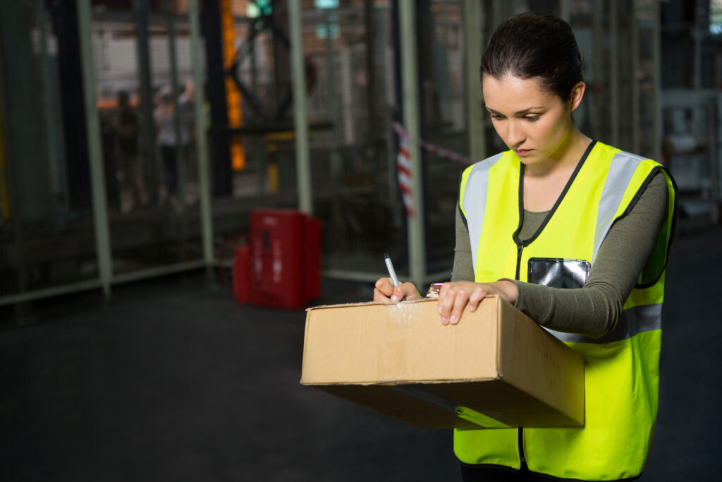 confident female worker writing on box in warehouse